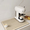 A white Smeez coffee maker sits on a beige drain mat with a white cup of coffee on it.