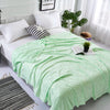 A light green bamboo fiber cooling blanket draped over a white bed with pillows and greenery.