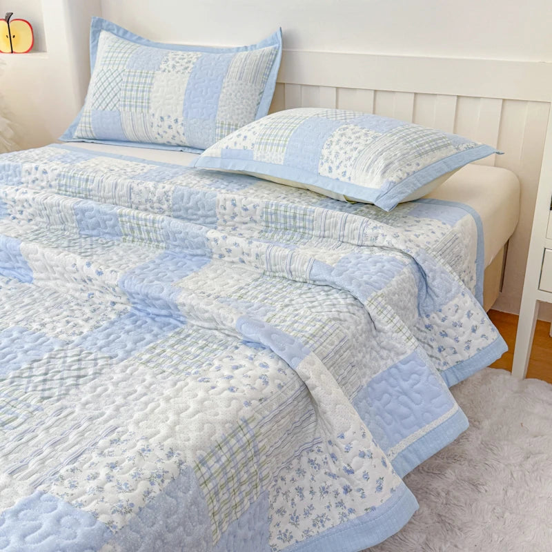 Light blue and white floral quilted bedspread with matching pillows on a white headboard.