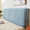 A light blue quilted fabric headboard cover is displayed on a bed, next to a framed picture.