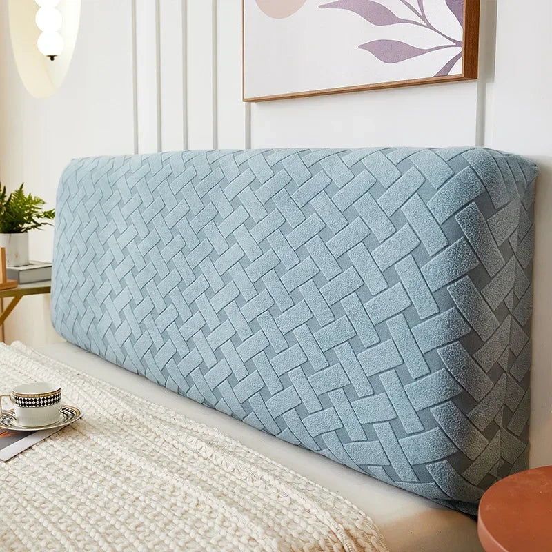 A light blue quilted fabric headboard cover is displayed on a bed, next to a framed picture.