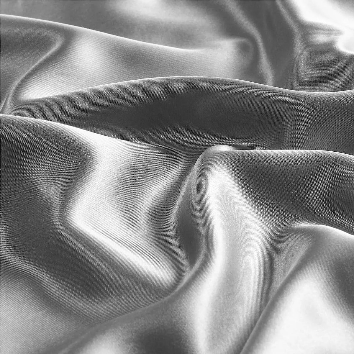 Close-up shot of two satin pillowcases draped and folded in a smooth, reflective gray fabric.