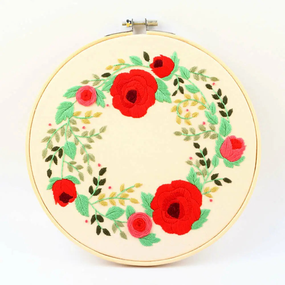 A round embroidery hoop featuring a floral wreath design in red and green thread.