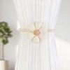 A pair of beige magnetic floral curtain tiebacks attached to a white pleated fabric.
