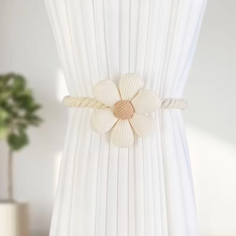 A pair of beige magnetic floral curtain tiebacks attached to a white pleated fabric.