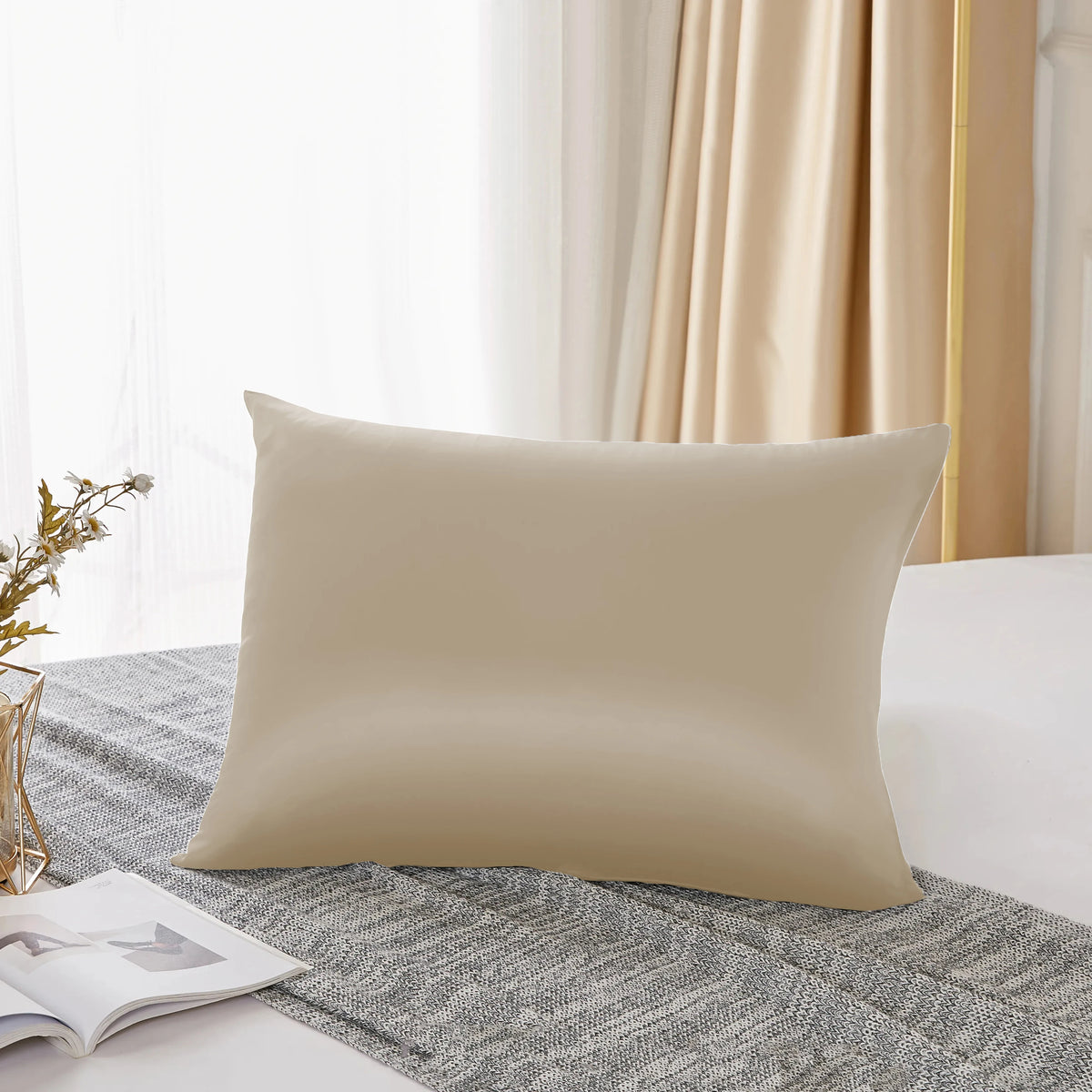 A beige pure mulberry silk pillowcase resting on a gray textured fabric near a window.