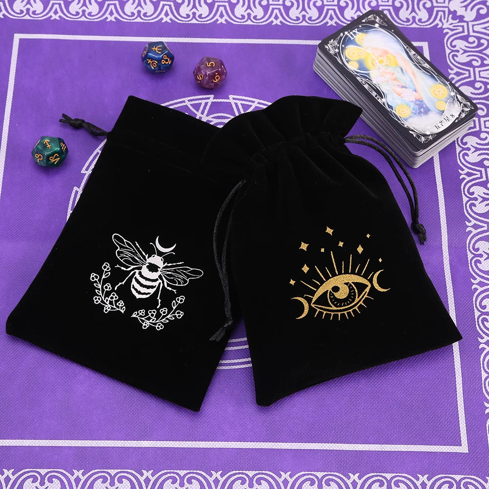 A black velvet tarot cards storage pouch with a silver bee and eye design, next to a stack of tarot cards.