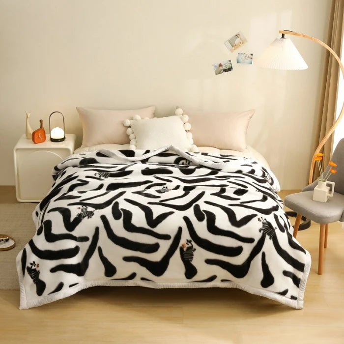 A white blanket with black zebra print lying on a bed, next to pillows and a lamp.
