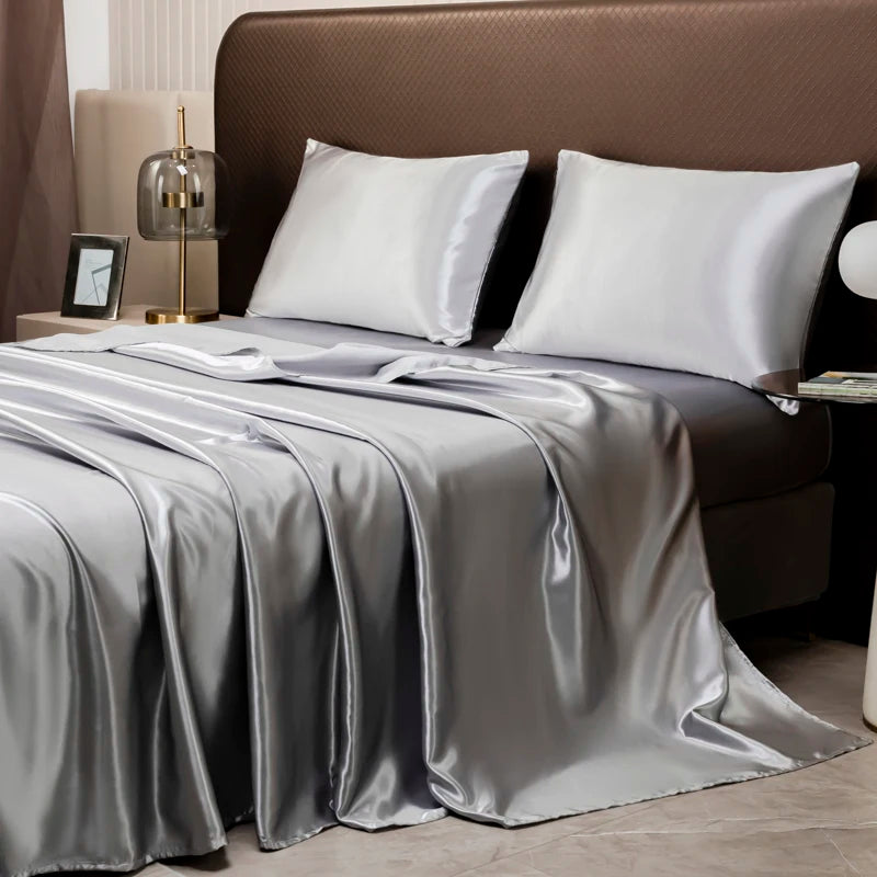 A luxury solid satin bedding set featuring silver gray sheets and pillows on a bed.