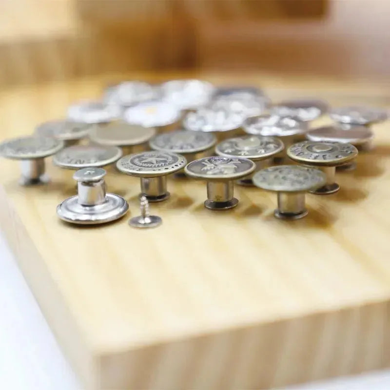 A collection of 30 silver jeans buttons laid out on a wooden surface.