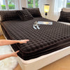 A dark brown fitted sheet set is laid out on a bed, with a hand touching the fabric.