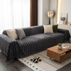 A dark gray bohemian striped sofa cover draped over a modern sofa in a bright living room.