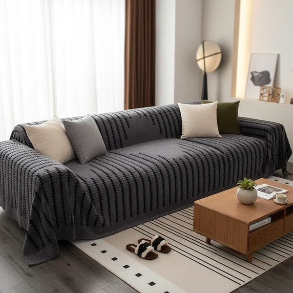A dark gray bohemian striped sofa cover draped over a modern sofa in a bright living room.