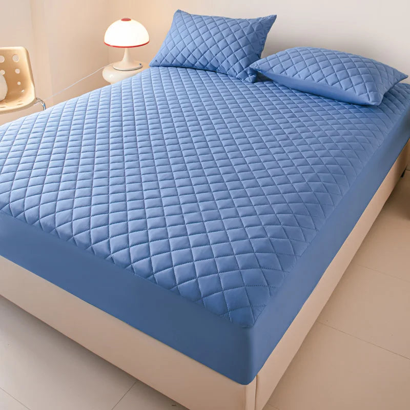 A light blue quilted mattress protector is shown on a bed, featuring a diamond pattern.
