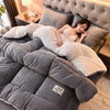 A woman is relaxing on a large gray quilted blanket with a fluffy white fleece lining in a bedroom setting.