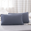 A stack of solid gray microfiber pillow covers on a bed with a checkered curtain in the background.