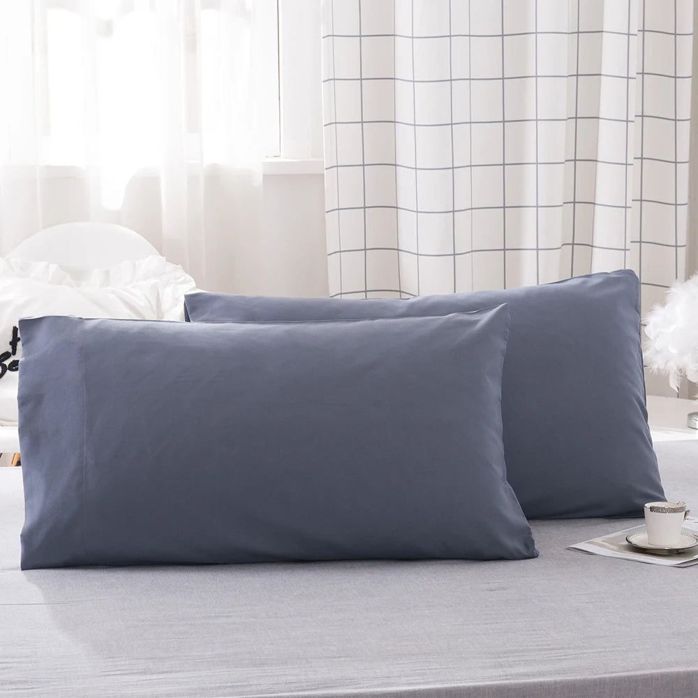A stack of solid gray microfiber pillow covers on a bed with a checkered curtain in the background.