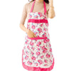 A woman wearing a pink floral print kitchen apron with pockets and an adjustable pink belt over a beige top.