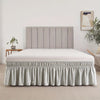 A modern bed featuring a light gray upholstered headboard and an adjustable elastic bed skirt with a ruffled trim.