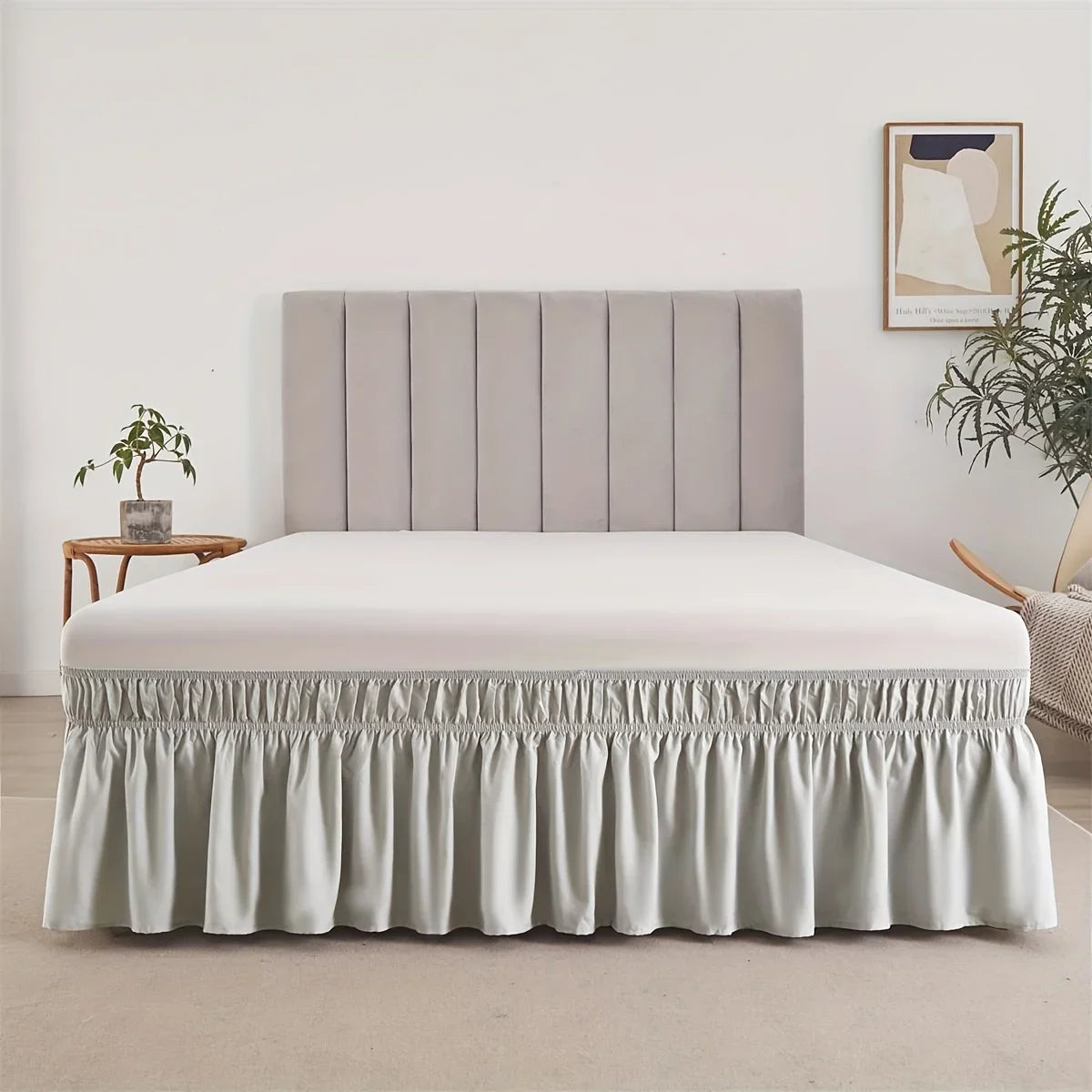 A modern bed featuring a light gray upholstered headboard and an adjustable elastic bed skirt with a ruffled trim.