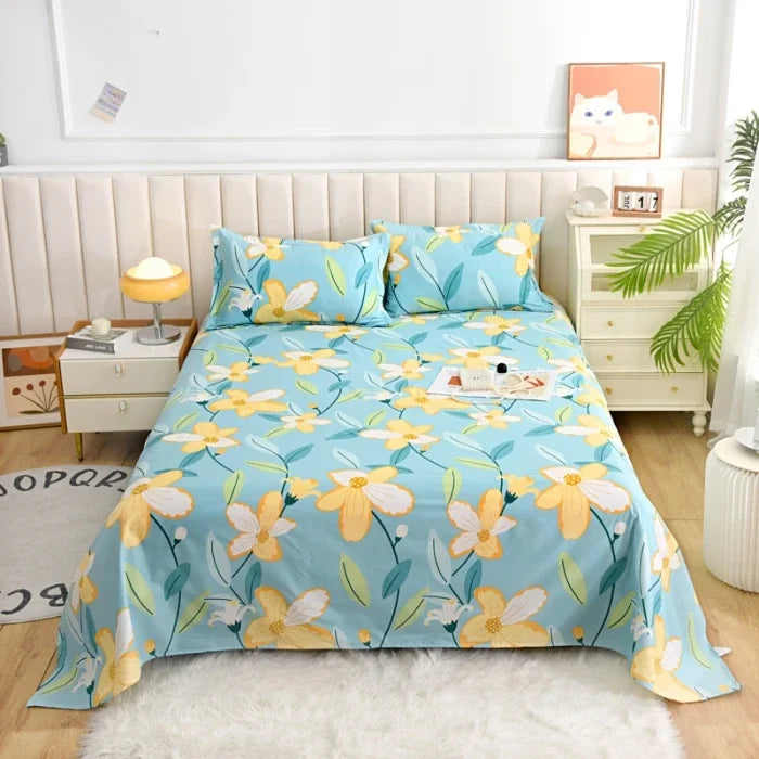 Light blue flat bed sheets with a yellow floral print displayed on a bed with a white headboard and bedside table.