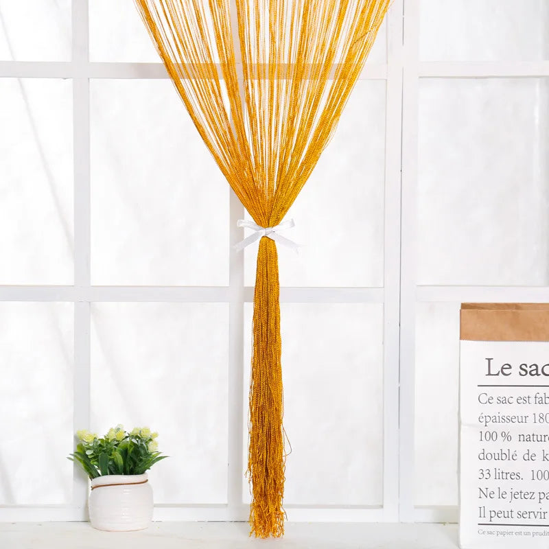 A bright golden thread curtain tie-back hanging from a window, with a small potted plant nearby.