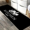 Black non-slip oil-proof floor mat with white text reading 'KITCHEN' placed on a wooden floor.