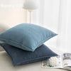 Two solid blue chenille throw pillows resting on a light surface next to an open book.