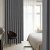 A heavy duty foldable room divider curtain in gray fabric hangs next to a window with sheer white curtains.