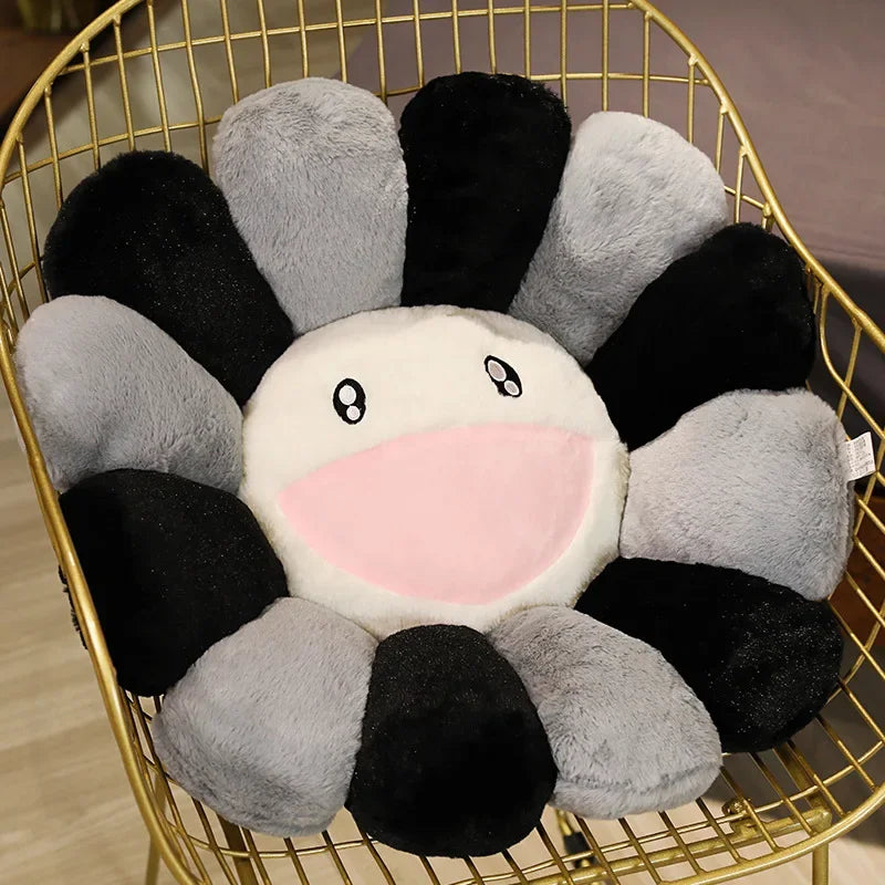 A cozy sunflower plush cushion with a smiling face, featuring black and gray fabric petals.