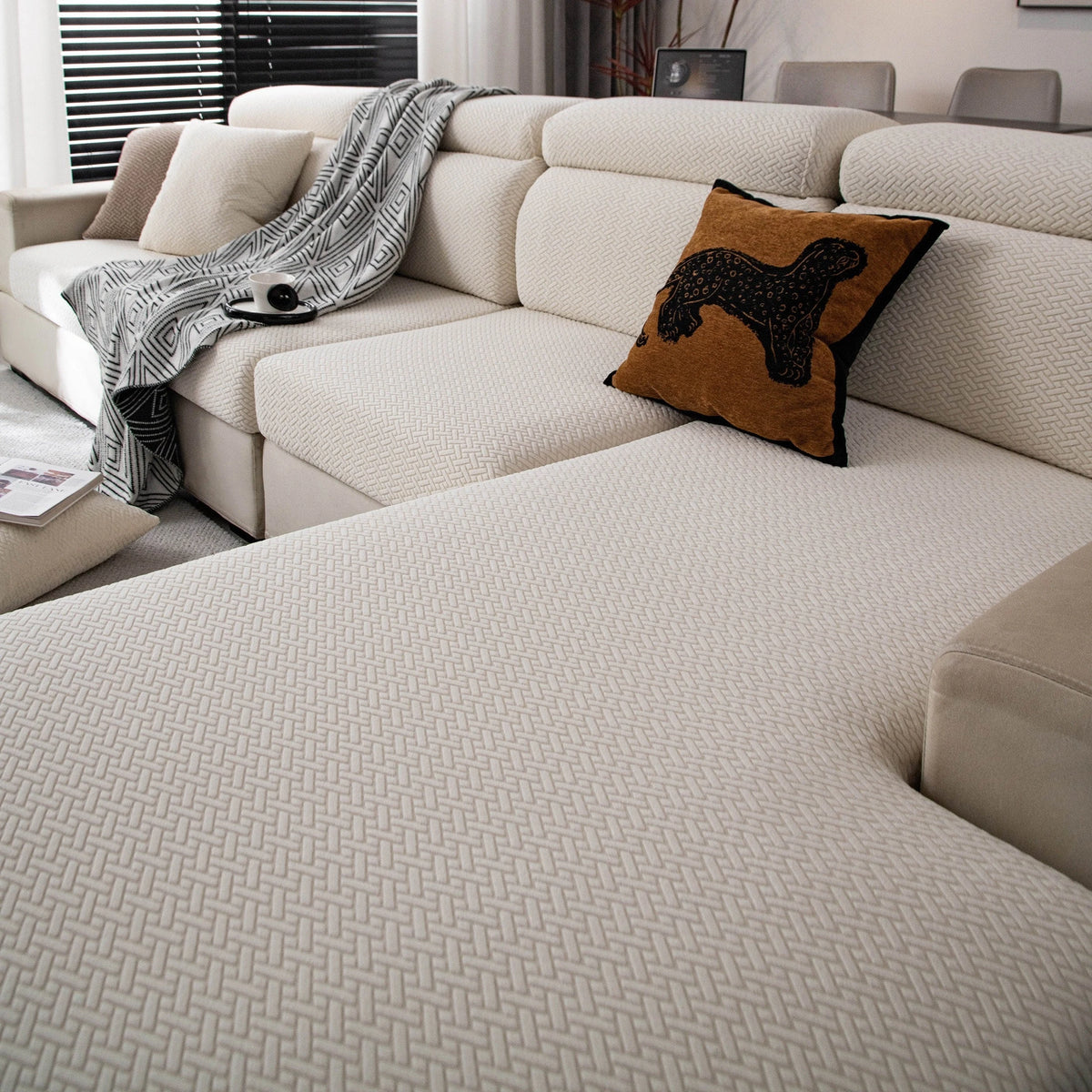 A light beige stretchy polar fleece sofa cover with a dark brown decorative pillow on a modern sofa.