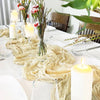 A bohemian gauze table runner draped on a white table with pillar candles and greenery.