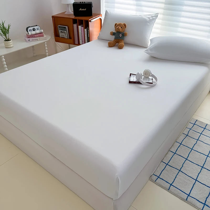 A white fitted bed sheet cover is displayed on a bed, next to a wooden shelf with books and a stuffed animal.