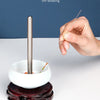 A hand is using a thin stainless steel beading needle to thread beads into a white bowl for DIY beading.