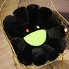 A black plush sunflower cushion with a bright green smile face is displayed in a gold wire basket.
