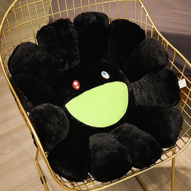 A black plush sunflower cushion with a bright green smile face is displayed in a gold wire basket.
