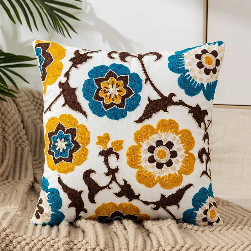 White canvas throw pillow cover embroidered with blue and yellow floral patterns on a beige knitted surface