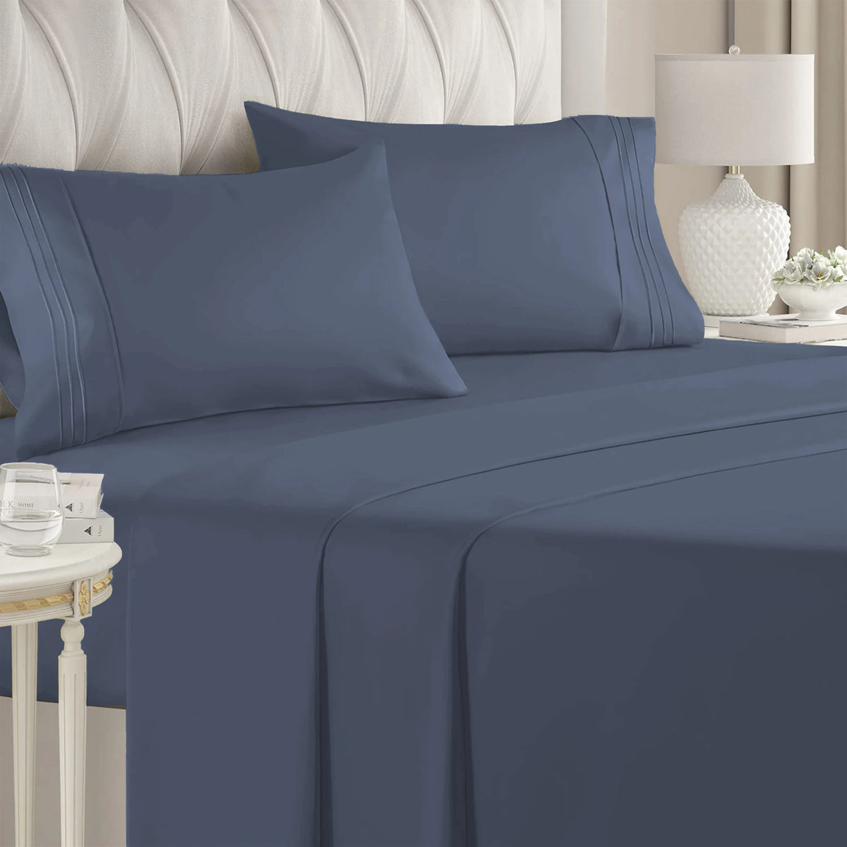 A set of four navy blue microfiber bed sheets with piping and deep pockets on a bed.