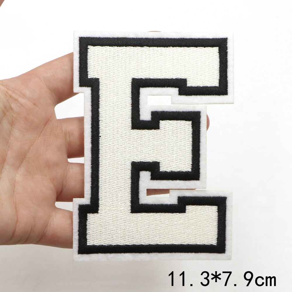 A hand holds a black and white letter patch shaped like the letter E.