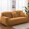 A mustard yellow stretch sofa cover with two accent pillows placed in a bright living room.