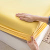 A hand is touching a bright yellow fitted bed sheet on a white bed frame.