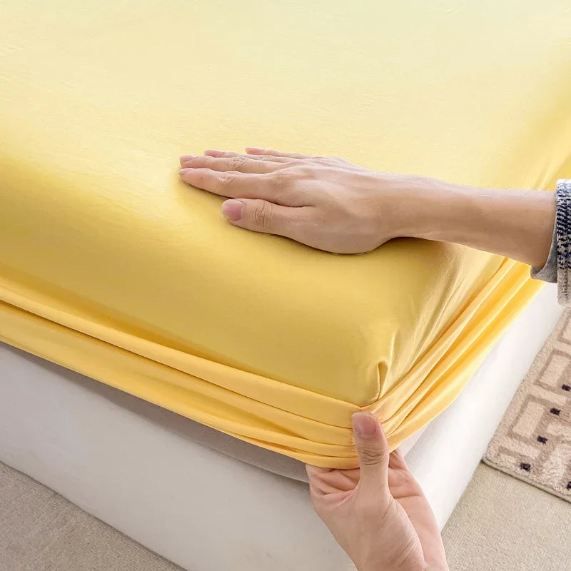 A hand is touching a bright yellow fitted bed sheet on a white bed frame.