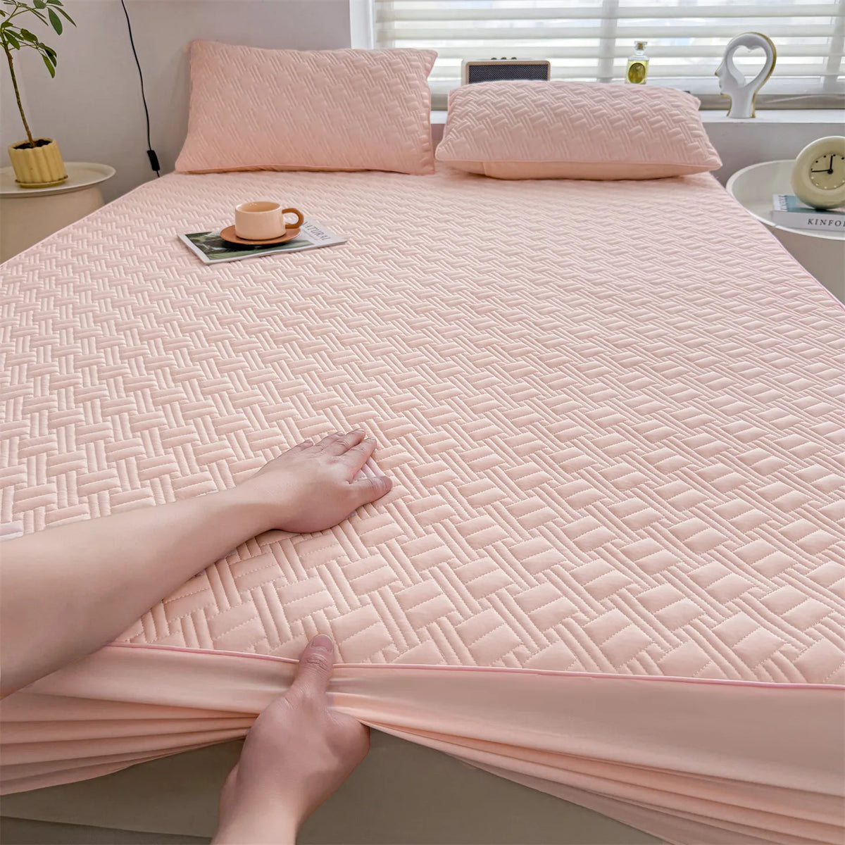 A close-up of a pink cooling spandex fitted sheet mattress protector being handled on a bed.