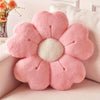 A pink plush daisy flower throw pillow with a white center resting on a light-colored surface.