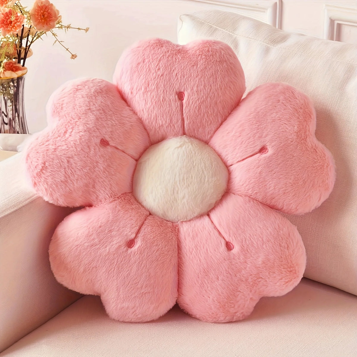 A pink plush daisy flower throw pillow with a white center resting on a light-colored surface.