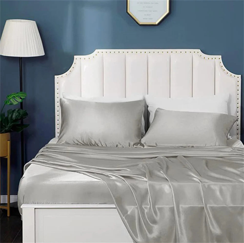 A white upholstered headboard with a satin gray pillowcase and sheet on a bed.