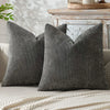 Two gray textured pillows resting on a light-colored surface next to a wooden table.