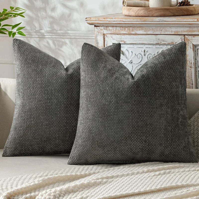 Two gray textured pillows resting on a light-colored surface next to a wooden table.