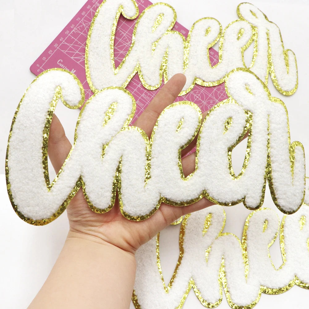 Hand holding a gold glitter embroidered patch spelling the word Cheer