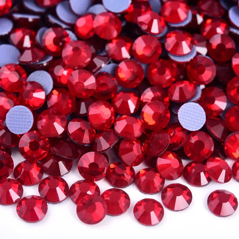 A close-up view of small, round, faceted red glass rhinestones scattered on a white surface.